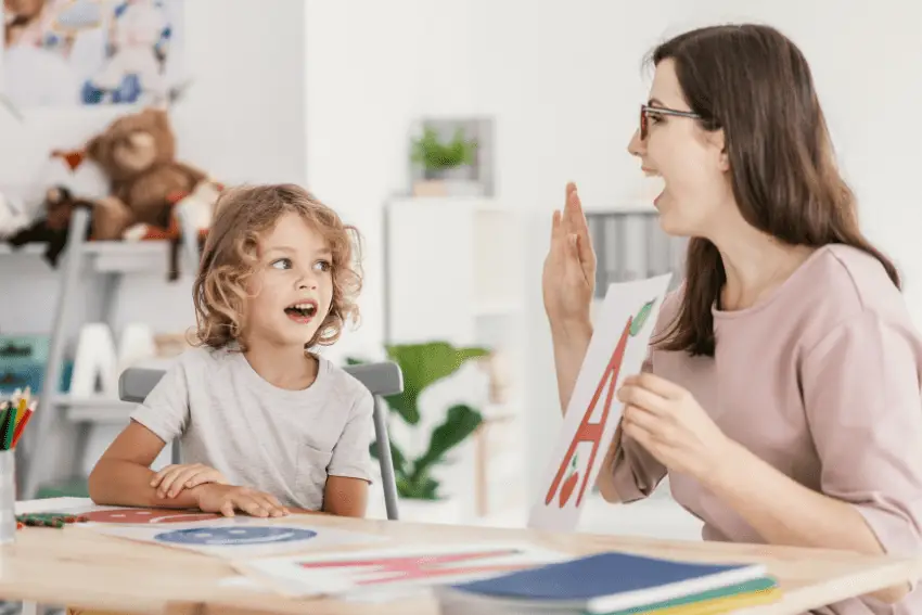 Courtney Schneider, SLP engaging with a young boy during a therapy session, using a clipboard with paper and colorful markers.