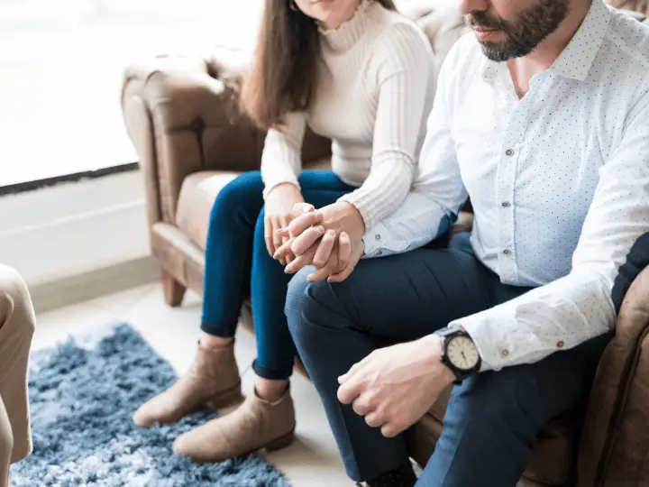 Couple sitting closely and holding hands during a counseling session, symbolizing support, connection, and relationship healing.