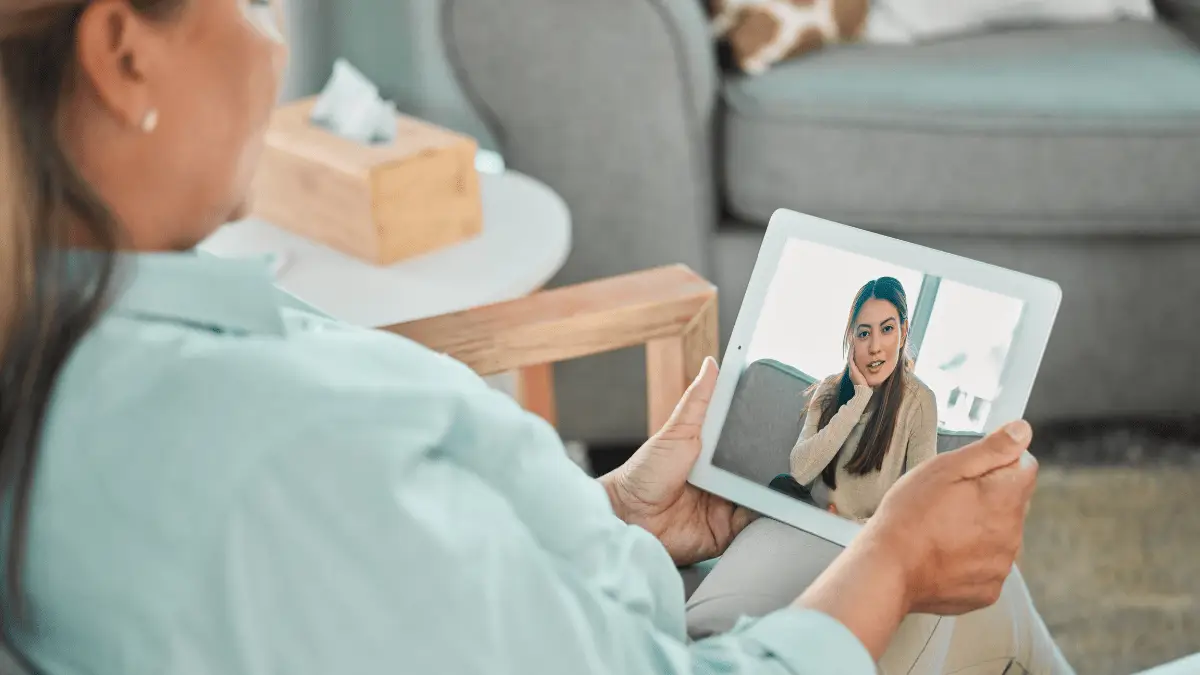Woman sitting in a quiet room during an online PTSD therapy session, looking calm and supported.